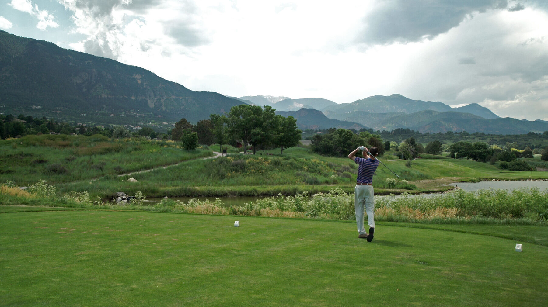 Man swinging on golf course with mountains in the background